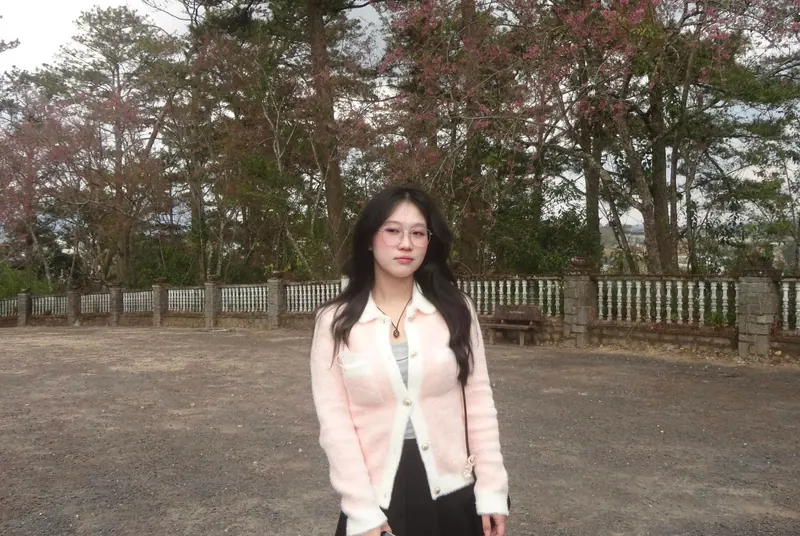 In a blush cardigan and glasses among pines and pink blossom trees.