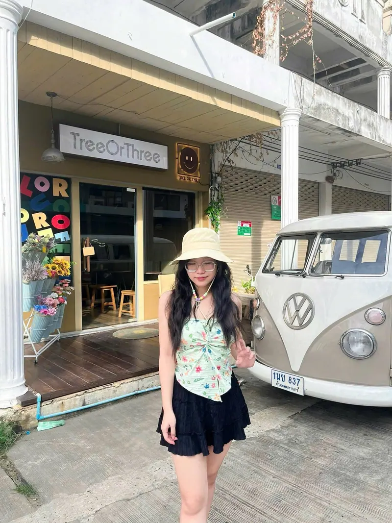 In a mint halter, clear glasses and a bucket hat outside a street café, making a peace sign.