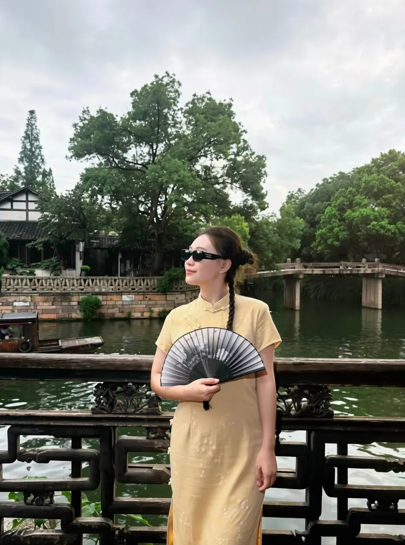 In profile with a painted fan, a wooden boat on the canal beside her.